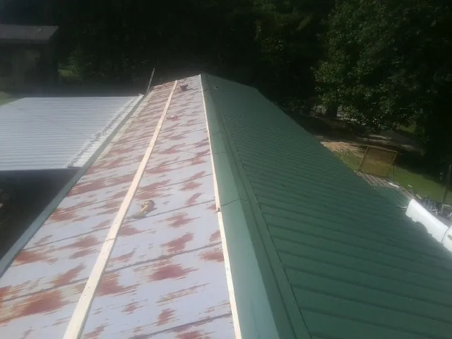 Old rusted panels beside newly installed green metal roofing — Wind Damage Roof Repair by Roofing Brothers in Butler